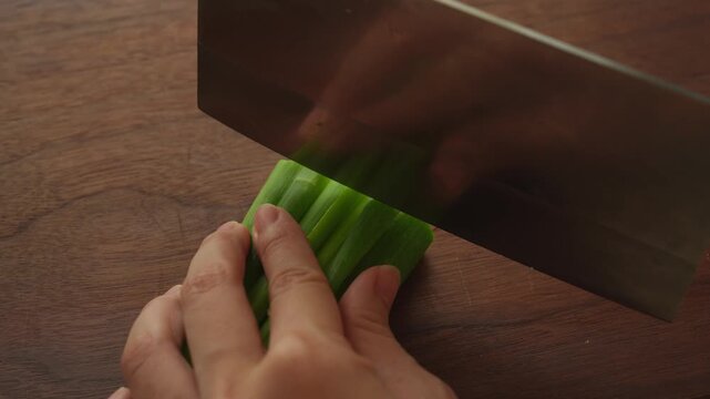 Chopping a bundle of green onion strips with a cleaver on a wooden board