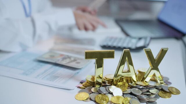 Gold TAX letters on a pile of coins with an office worker handling financial documents and a calculator in the background, illustrating tax calculation and planning.