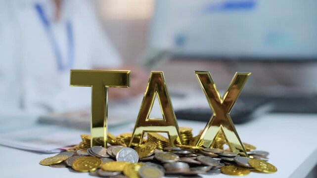 Gold TAX letters and coins in focus on an office desk while a worker handles financial paperwork in the background, symbolizing tax liabilities and payment planning.