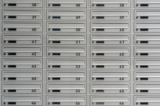 Detailed view of multiple gray steel postal boxes arranged in symmetrical rows and columns, featuring apartment numbers, key locks and letter slots in a residential building