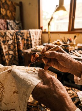 Close-up of artisan hand applying hot wax on fabric using canting tool to create traditional Indonesian batik cloth