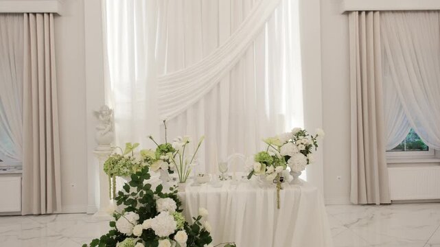 An elegant wedding reception table decorated with white hydrangeas and green accents in a bright white room