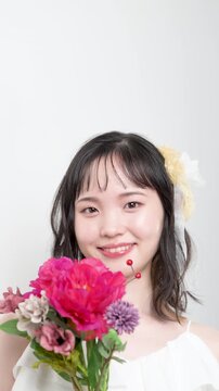 白いウェディングドレスを着てピンクのブーケを持つカメラ目線の若い20代の日本人女性の花嫁、結婚式やフォトウェディングの幸せと喜びを表現したブライダルイメージの動画