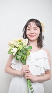 [スロー]白いウェディングドレスを着てブーケを持つカメラ目線の若い20代の日本人女性の花嫁、結婚式やフォトウェディングの幸せと喜びを表現したブライダルイメージの縦動画