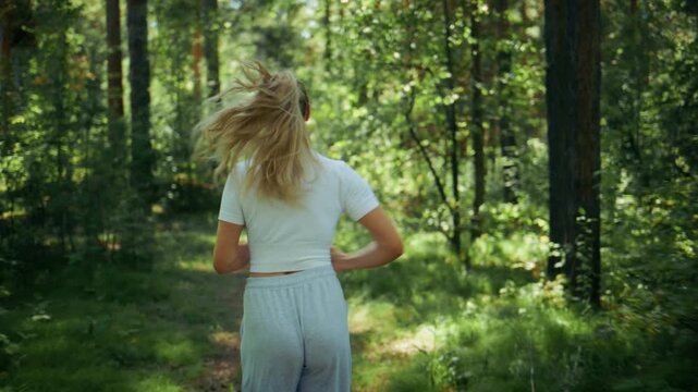 Young woman runs through sunlit forest path. Her hair flows freely behind her. Movement captures joyful, carefree energy. Perfect for fitness, nature, or wellness projects