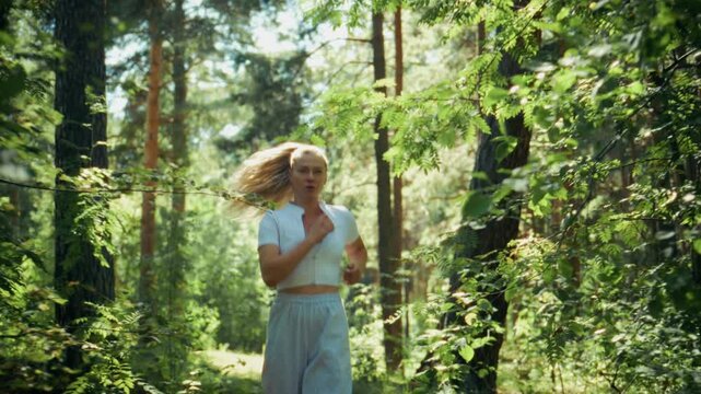 Woman runs through lush green forest. Sunlight filters through tall trees. Her hair flies as she moves. Scene shows active, healthy lifestyle. Perfect for fitness, nature, or wellness content