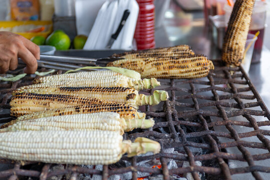 Hands Turning Corn Cobs on a Street Grill