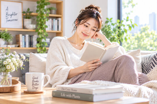 日差しの入る自宅のソファで読書を楽しむ女性