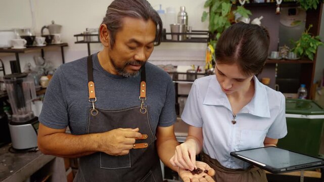 Two cafe professionals examining coffee beans together, illustrating workplace mentoring, barista training, knowledge sharing, and quality evaluation in a specialty coffee business.

