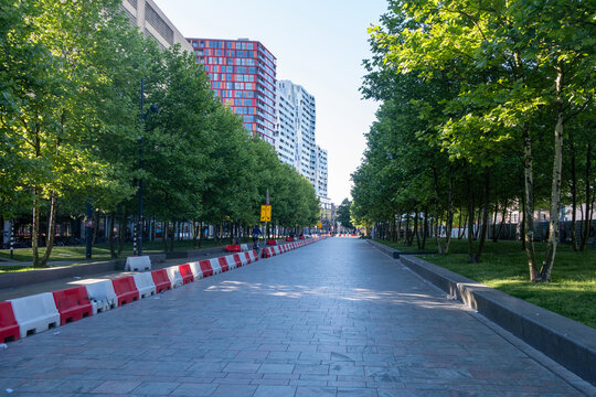 Red and white traffic barriers on a tree-lined street with modern towers in Rotterdam, Netherlands