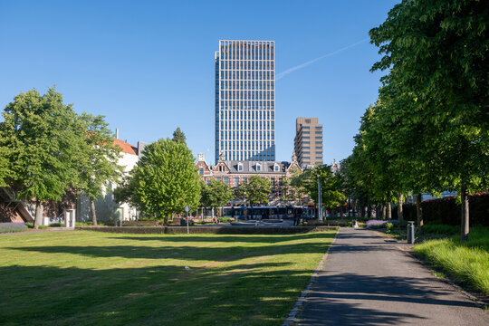 Park path beside green lawns, modern towers and historic brick facades in Rotterdam, Netherlands