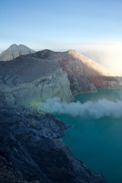 Turquoise acidic crater lake with sulfur smoke and volcanic mountains at Kawah Ijen, East Java, Indonesia