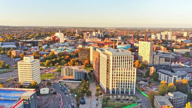 Coventry city centre towers, rooftops and streets glowing at golden hour near the railway station in the West Midlands, England, drone ascent