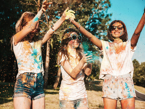 Three happy beautiful girls making party at Holi colors festival in summer time.Young smiling women friends having fun after music event at sunset.Positive models going crazy in sunglasses at sunset