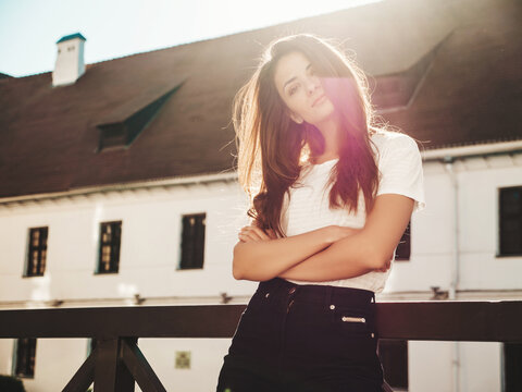 Closeup portrait of beautiful smiling brunette model. Trendy female posing in the street background. Funny and positive woman having fun outdoors at sunset. Crossed arms