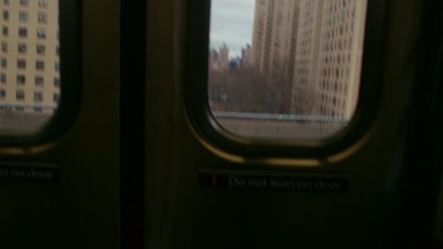 Apartment buildings slide past the windows of subway doors, with dark carriage panels framing the changing view of the New York neighborhood. A winter view of New York City, United States.