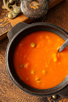 Bowl of vegetable soup with a vintage leather journal, fountain pen and a pocket fob watch on an aged leather background backdrop