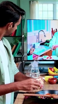 Young Indian man learning to prepare traditional modak dumplings in a modern kitchen while watching a cooking recipe on TV, Indian cuisine, homemade food and culinary skills concept.