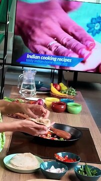 Young Indian woman learning to prepare traditional modak dumplings in a modern kitchen while watching a cooking recipe on TV, Indian cuisine, homemade food and culinary skills concept.