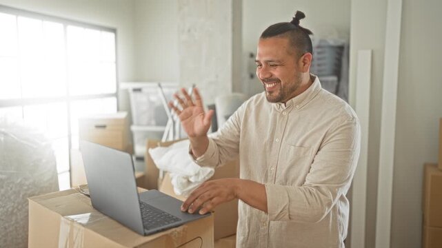 Man smiling and typing on a laptop placed on moving boxes with hands on keyboard in a building filled with packed boxes during a move; optimism remote work.