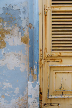Weathered Yellow Louvered Door Panel Beside Light Blue Painted Wall Frame with Flaking Paint and Rusting Hinges