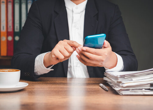 Businessperson using smartphone at office desk with documents 