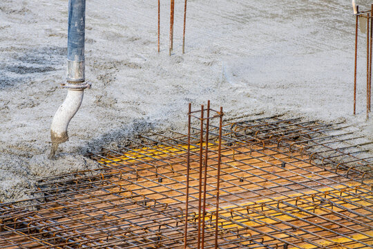 Fresh concrete is poured over steel reinforcement mesh at a construction site, showing foundation work, rebar installation, and structural engineering in progress.
