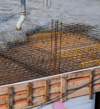 Fresh concrete is poured over steel reinforcement mesh at a construction site, showing foundation work, rebar installation, and structural engineering in progress.