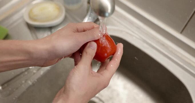 Close-up male hand wash rinse tomato under tap water in sink. 4K 10-bit