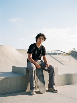 Teenage skateboarder sitting at skatepark with medal