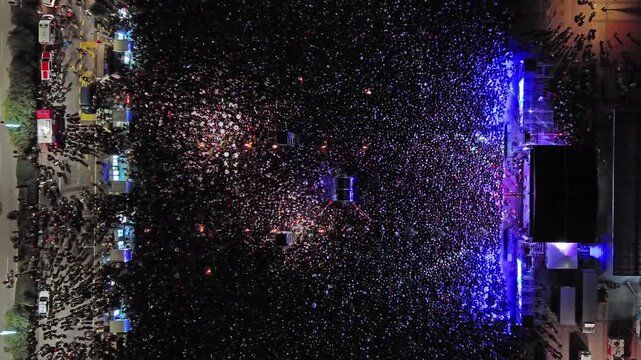 Aerial top view of crowd at night music concert. People gathered at festival outdoor stage with lights and screens, 4k