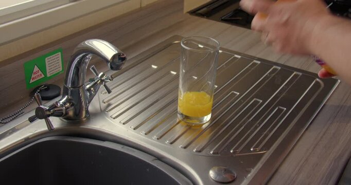 Zoom Shot of orange squash cordial being made in a glass on the kitchen sink.