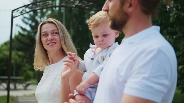 Happy family explores outdoors together. Mother and father hold toddler child. Child points excitedly at something in distance. Family smiles warmly while enjoying nature. Perfect for parenting