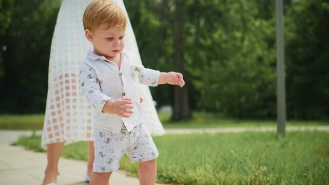 Young boy walks confidently on path. He wears light-colored outfit with pattern. Green trees surround paved walkway. Soft focus background adds calm atmosphere. Scene ideal for family, childhood
