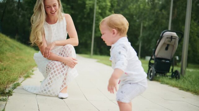 Mother kneels, watching baby crawl on path. Mother smiles warmly. Baby explores with curiosity. Stroller rests nearby. Perfect for parenting, family, or outdoor lifestyle content