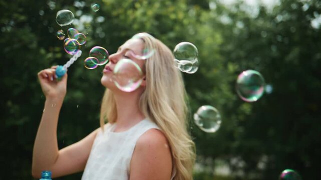 Young woman blows colorful bubbles in a sunlit park. She smiles joyfully, eyes closed, enjoying the moment. The bubbles float gently around her, catching light. Perfect for summer, childhood