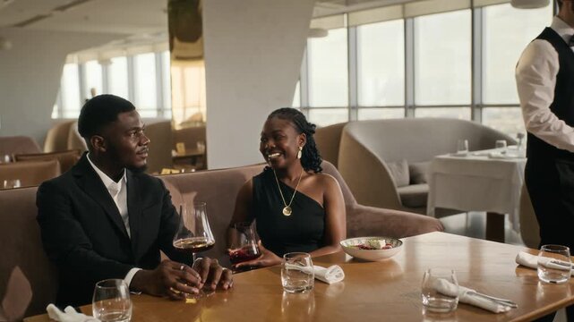 African American young adult couple receiving food from waiter at restaurant dinner date. Perfect for fine dining commercials, hospitality branding, and luxury lifestyle marketing