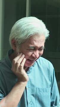 Old asian senior man with oral hygiene issue suffering from toothache, indoor home scene