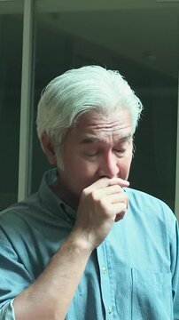 50s southeast asian man with white hair suffering a runny nose from cold or flu, home indoor scene