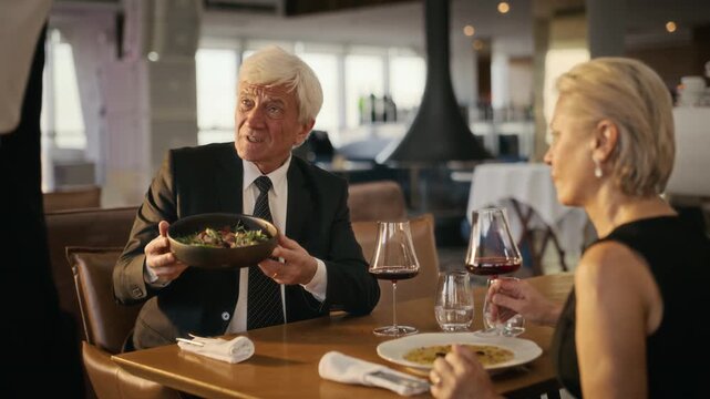 Senior Caucasian man returning meal to waiter while dining with senior Caucasian woman in restaurant. Ideal for hospitality customer service training and senior lifestyle marketing campaigns