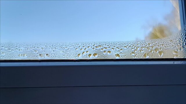 Accumulated water droplets and condensation on double glazed window glass surface with clear blue sky visible above, indoor humidity defect and temperature difference concept stock asset.