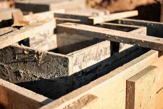 Concrete fills timber formwork for a foundation at a construction site, with wood boards and tools visible during the building work