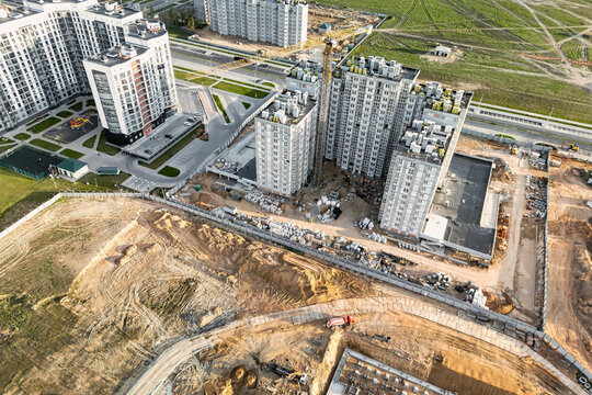 An aerial view of apartment buildings, paved roads, and earthworks at a residential development site, with a construction vehicle on the ground