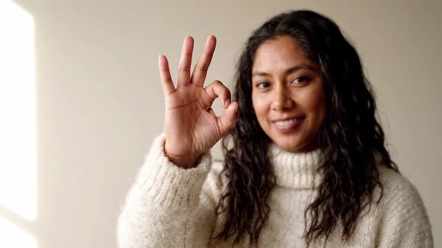 Smiling woman making OK hand gesture indoors. Positive communication and approval concept. Friendly expression, affirmation and agreement. Close-up portrait with copy space.