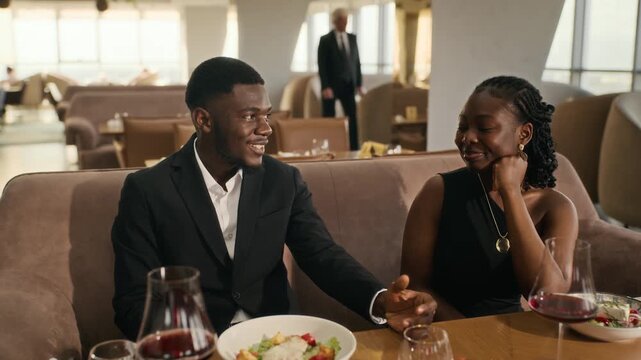 Waiter serving dish to young adult African American couple enjoying dinner in luxury restaurant. Footage suitable for fine dining advertisements and dating campaigns
