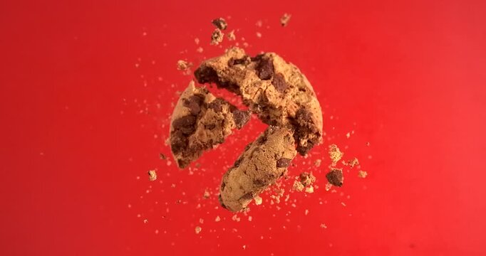Chocolate chip cookie falling with crunchy crumbs on red background in slow motion