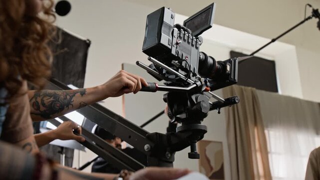 Young adult man operating cinema camera on crane during studio shoot with Caucasian female film director. Ideal for media production promos, cinematography masterclasses, and filmmaking campaigns
