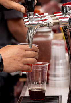Hand pours dark beer from tap into plastic cup