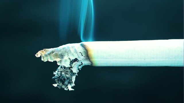 Burning cigarette with swirling blue smoke close up