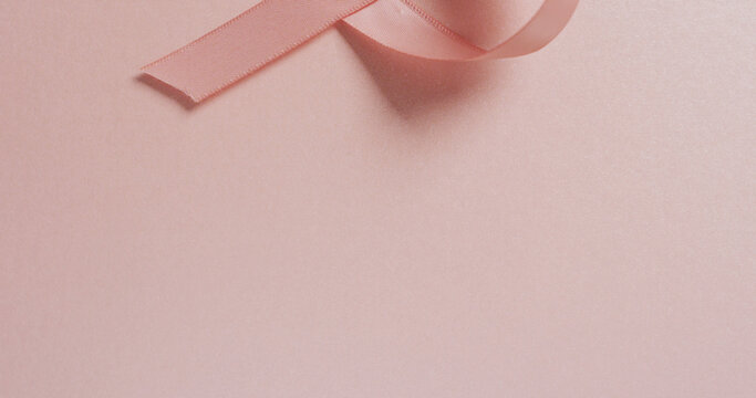 Image of pink breast cancer ribbon and shadow on pale pink background